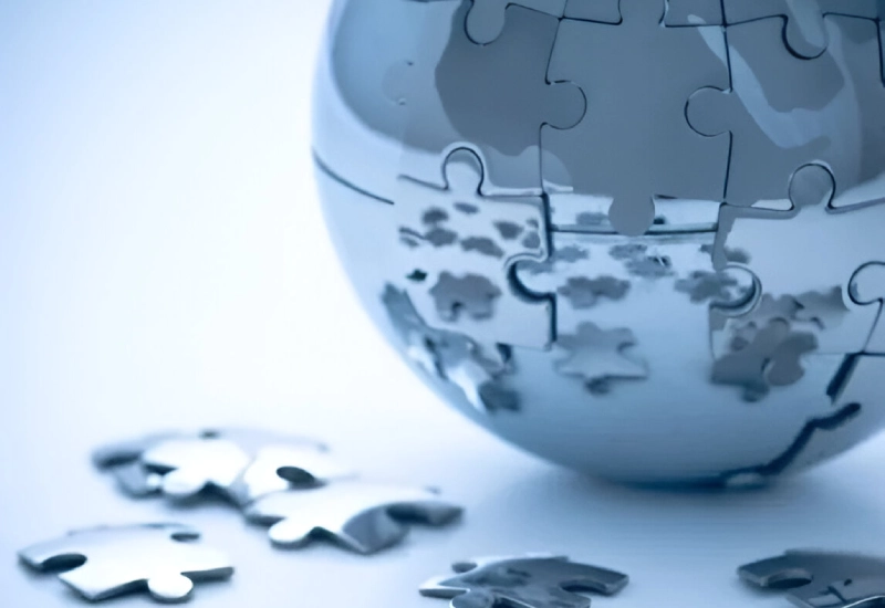 Close-up of a metallic globe made of interlocking puzzle pieces, with several loose pieces scattered around it on a light-colored surface. The setup captures the reflective effect, symbolizing the intricate pathways to revenue maximization.