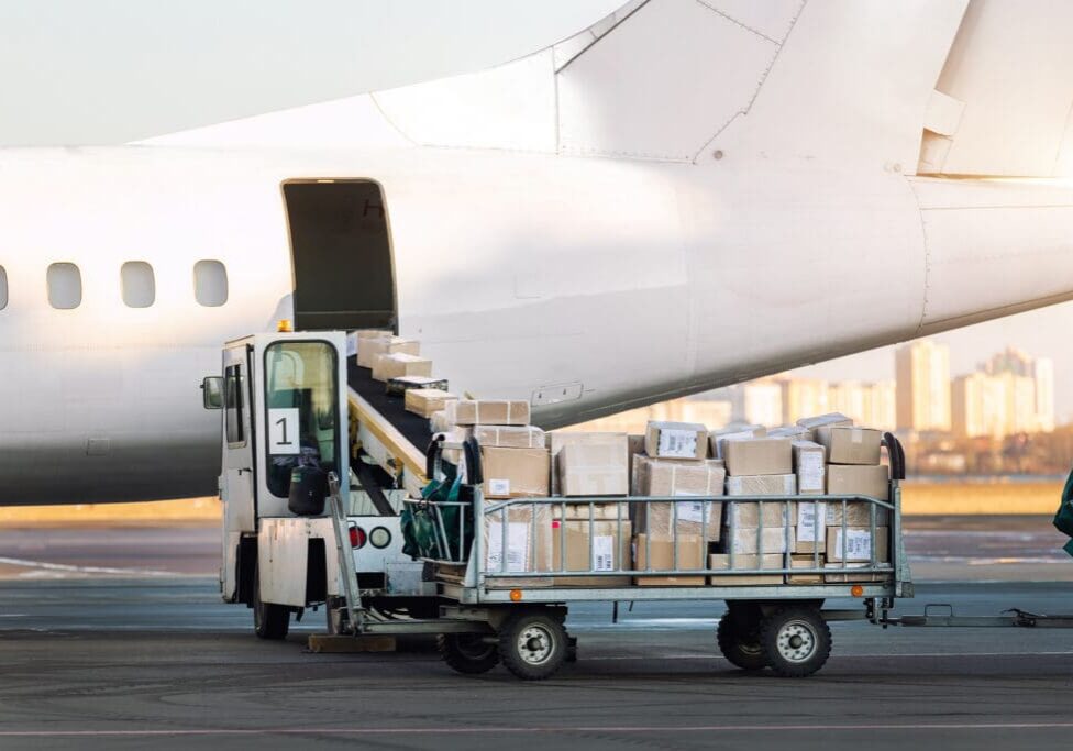 Close-up detail view of cargo cart trolley full with commercial parcels against turboprop cargo plane. Air mail shipping and logistics. Import export operations. Commercial charter flight service.