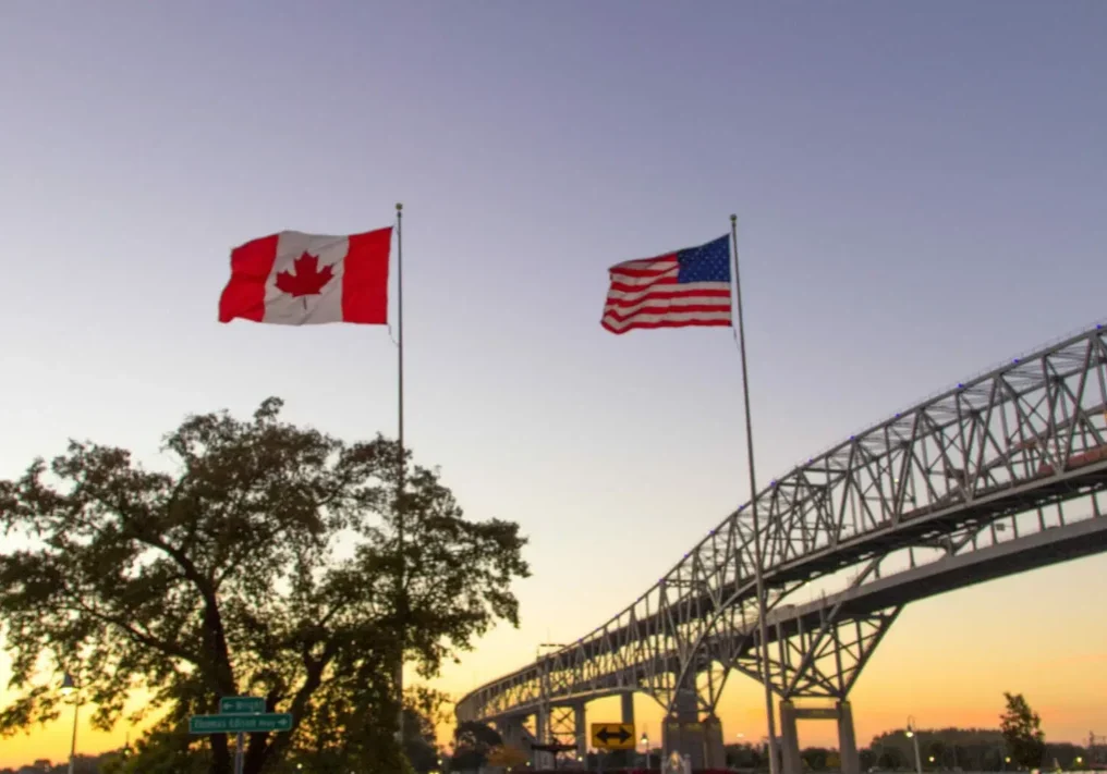 Canadian and US flags at sunset bridge.